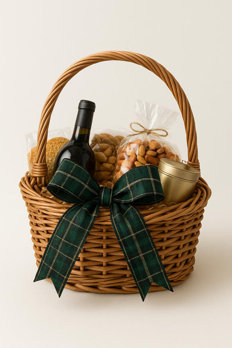 Wicker gift basket with wine bottle, snacks, and a plaid bow on a white background