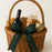 Wicker gift basket with wine bottle, snacks, and a plaid bow on a white background
