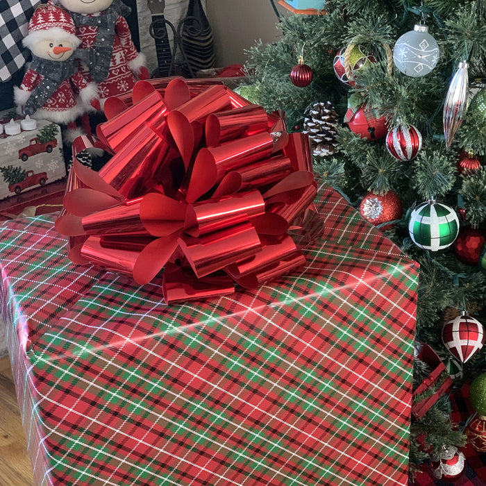 large metallic red bow on a large gift box in front of a Christmas tree
