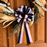 A decorative dried flower wreath with a large black and pink striped pull bow, hung on a brown wooden door.
