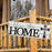 Wooden sign with 'bless this HOME' text and cross design on a rustic house