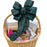 A wicker gift basket filled with assorted packaged snacks and treats, topped with a large green plaid bow. Visible items include a box of Brisket seasoning, a box of Rustic Bakery cookies, a bag of Ritz crackers, and other candy and snack packages, all photographed on a plain white background.