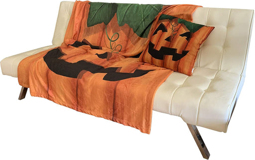 An orange and black jack-o'-lantern themed throw blanket and matching pillow set draped over a white tufted futon sofa.